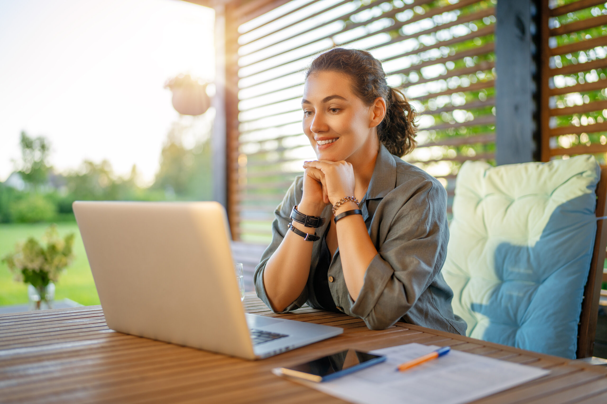 Happy young woman is working sitting on the patio in summer.